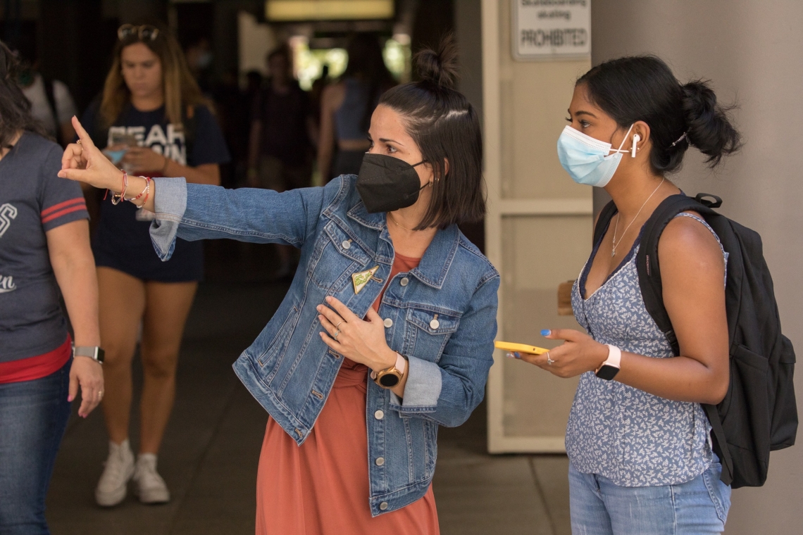 a woman wearing a mask points while another one woman in a mask looks in that direction